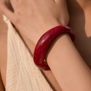 Dettaglio di un ampio bracciale rigido in resina rosso scuro con trama marmorea al polso