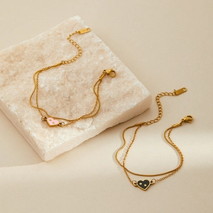 Double-layered gold stainless steel bracelets with pink and black heart charms on marble
