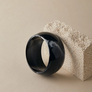 Gros plan d'un large bracelet en résine noire brillante sur un support en pierre