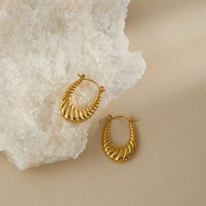 Dettaglio macro di orecchini croissant dorati con trama a spirale vintage su pietra bianca