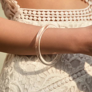 Moderner minimalistischer runder Armreif aus klarem Acryl auf Spitzenkleid-Hintergrund
