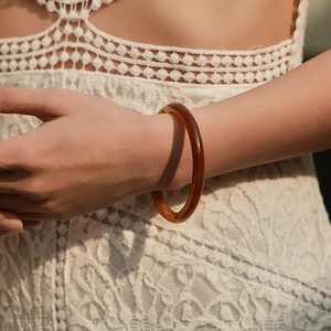Nahaufnahme des bernsteinfarbenen Acryl-Armreifs am Modell mit weißem Spitzenkleid
