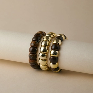 Dettaglio di tre braccialetti elastici con perle occhio di tigre e accenti in metallo oro