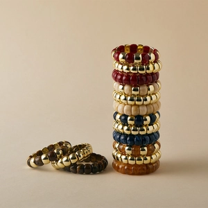 Dettaglio di bracciali elastici boho con perle dorate e pietre in resina colorata