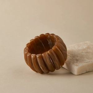 Macro detail of wide amber resin elastic bracelet leaning against a natural stone