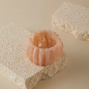Close-up of pink marbled acrylic bead bracelet on textured stone surface with soft lighting