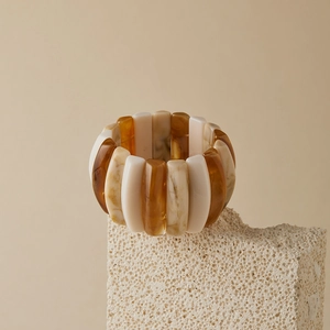 Artistic detail of a wide amber marbled resin cuff bracelet on stone pedestal
