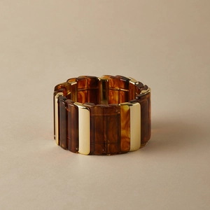 Détail d'un large bracelet en résine ambrée avec des accents en métal doré poli