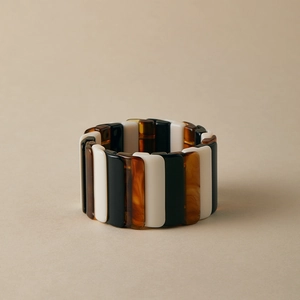 Détail d'un large bracelet extensible avec carreaux en résine noirs, blancs et ambre