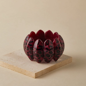 Close-up of a wide elastic leopard print resin bracelet on a beige stone pedestal
