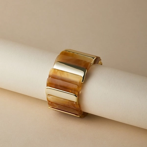 Détail d'un bracelet jonc épais en résine et métal doré poli sur un support neutre