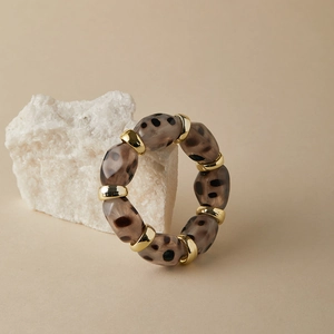 Leopard print acrylic beaded bracelet with polished gold metal rings on stone display