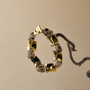 Detail of leopard print beads and polished gold metal charms on an elastic bracelet