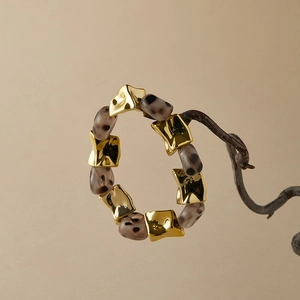 Close-up of leopard print acrylic beads and irregular gold metal links on dry wood