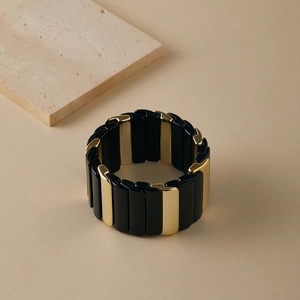 Détail d'un bracelet élastique à carreaux noir et or sur un plateau en pierre naturelle