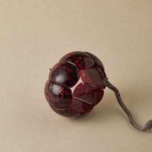 Detail of red leopard print resin bangle with block segments on a rustic wood branch