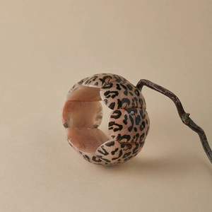 Detail of leopard print resin bracelet with elastic petal-shaped segments on wood branch