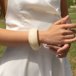 Minimalist creamy white acrylic resin bangle worn by model against a soft green lawn background