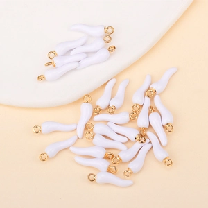 Macro detail of white enamel cornicello chili charms with gold loops for DIY jewelry making