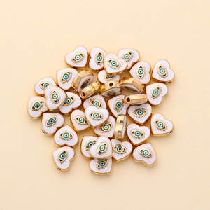 Close-up of heart-shaped evil eye spacer beads with gold trim and white enamel for DIY jewelry