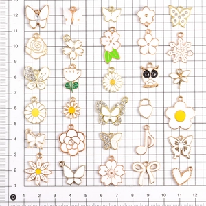 Detailansicht verschiedener weiß-goldener Emaille-Anhänger auf einem Messgitter