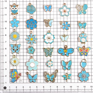 Blaue Emaille-Anhänger im Set mit Schmetterlingen und Blumen auf einer Matte