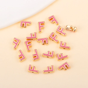 Détail macro de la perle lettre F en alliage doré avec émail rose pour bijoux faits main