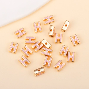 Détail macro d'une perle lettre H en émail rose et finition dorée pour bijoux DIY