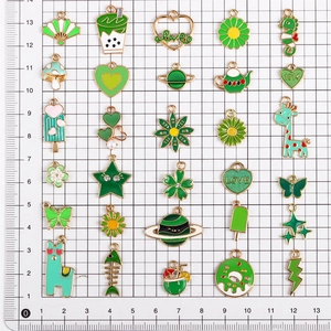 Grüne Emaille-Anhänger auf 1x1cm Raster zeigen verschiedene Formen und Abmessungen