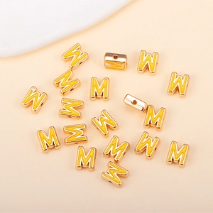 Détail de perle lettre M jaune émaillée avec bordure dorée pour création de bijoux