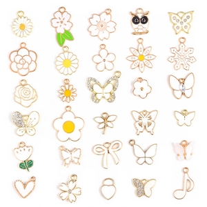 Makroaufnahme von 25 weißen Emaille-Blumen- und Schmetterlingsanhängern für DIY-Schmuck