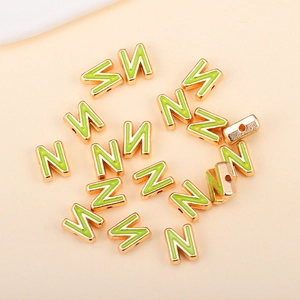 Gros plan d'une perle lettre N en émail vert avec bordure dorée pour bijoux DIY