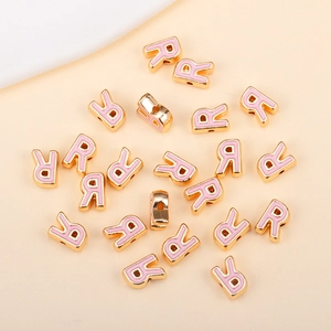 Détail macro de breloques lettre R dorées avec émail rose pour la création de bijoux