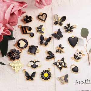 Sortierte schwarz-goldene Legierungsanhänger für DIY-Schmuck auf weißem Stoff präsentiert