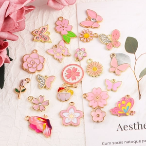 Makro-Detail von rosa Emaille-Blumen und Schmetterling-Anhängern für DIY-Schmuckbau