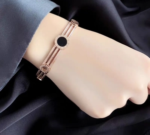 Close-up of rose gold roman numeral bangle with triple chain and black enamel detail