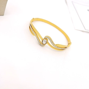 Detailaufnahme des goldenen Wellenarmbands mit Zirkonia-Steinen und modernem Design