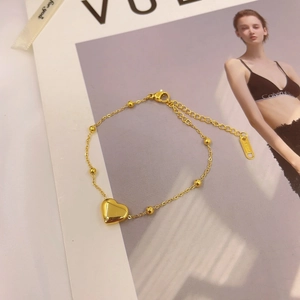 Minimalist gold titanium heart bracelet with small beads and lobster clasp on magazine