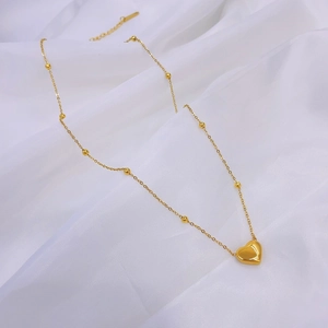 Dettaglio macro della collana con pendente a cuore dorato su tessuto bianco