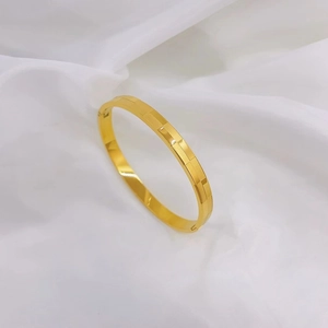 Minimalist checkered gold titanium steel bangle on a soft white fabric background