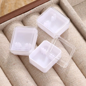 Tre mini scatole bianche per gioielli con coperchi trasparenti su vassoio beige