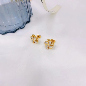 Close-up of golden windmill earrings with white zircons on soft textured fabric