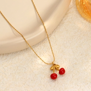 Elegante collar dorado con colgante de cereza y cuentas rojas sobre un fondo texturizado