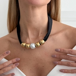 Detailed view of a black choker necklace with large pearl and polished gold beads