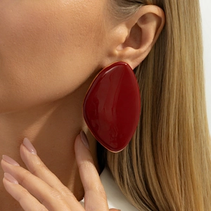 Close-up of oversized retro gold-framed earrings with deep red enamel drip glaze