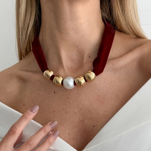 Detail of red velvet choker featuring a central white pearl and polished gold beads