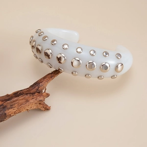 Detail of white resin cuff bracelet with three rows of silver rivets on wood