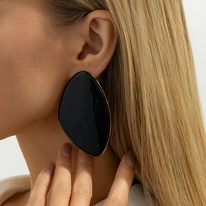 Macro shot of large black enamel geometric earrings with gold trim on model ear