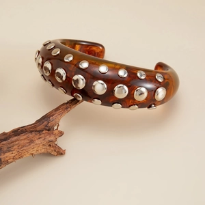 Detail of amber resin cuff with silver rivets on dry branch, vintage punk style