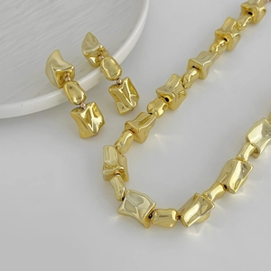 Gouden chunky ketting en druppeloorbellen met onregelmatige vierkanten op wit oppervlak